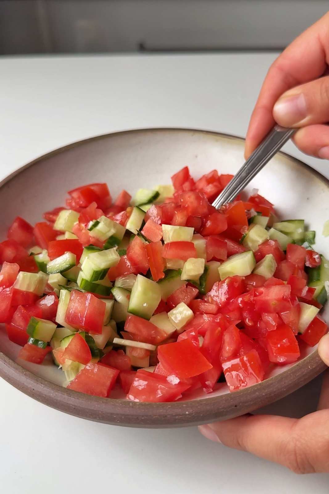 Stirring a bowl of freshly diced tomatoes and cucumber with a fork.
