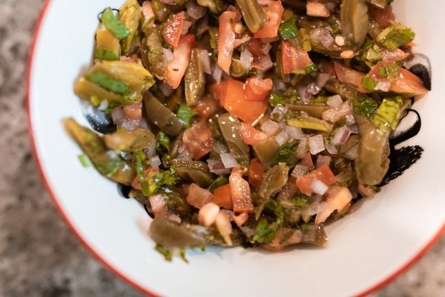 Ensalada de nopales, a Mexican cactus salad with tomato, red onion and cilantro in a white bowl.