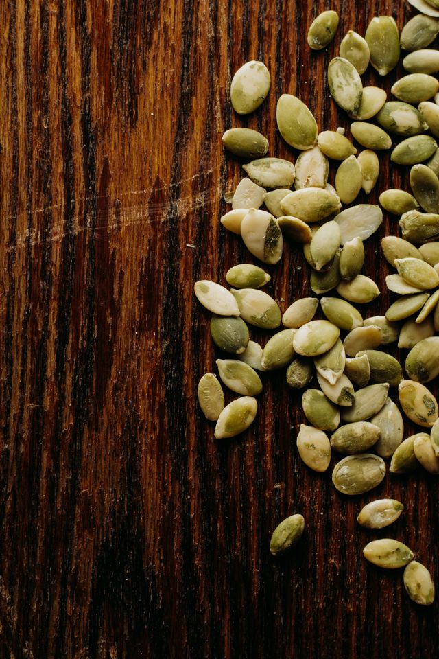 Raw green pepitas, or pumpkin seeds, scattered on a dark wooden board.