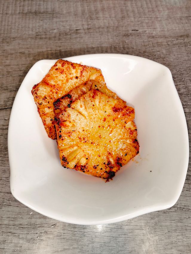 Grilled pineapple slices with charred caramelised edges and a dusting of chile powder on a white plate.