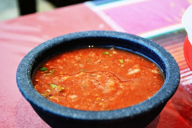 Chunky red salsa roja flecked with cilantro in a stone bowl on a taqueria table.