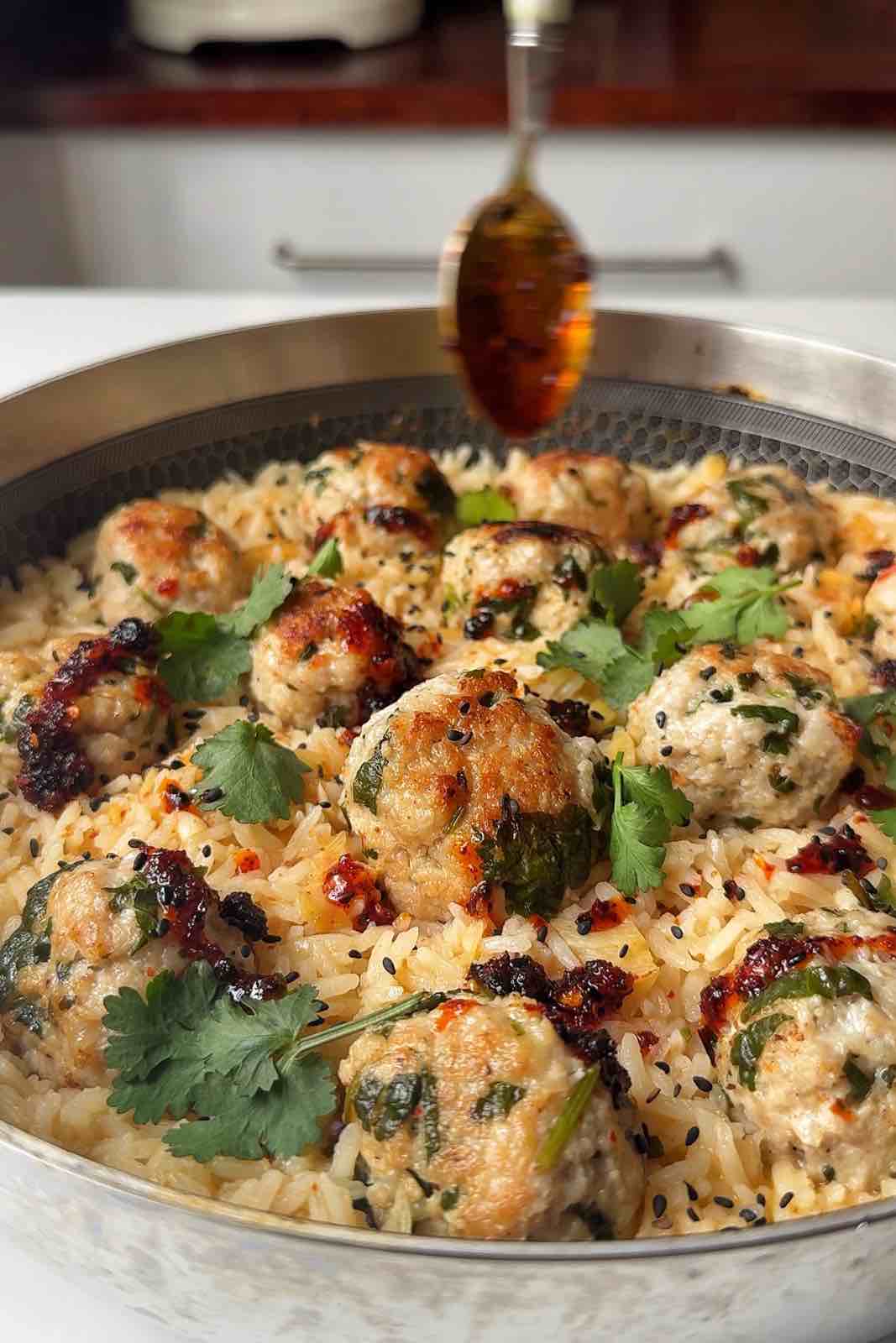 Drizzling chili oil over Thai chicken meatballs with rice one pot.