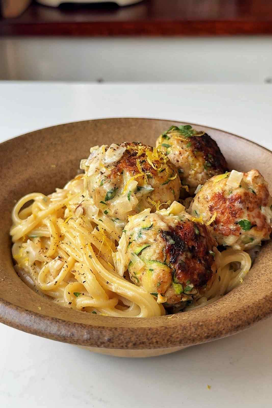Spaghetti with zucchini chicken meatballs in a brown bowl.