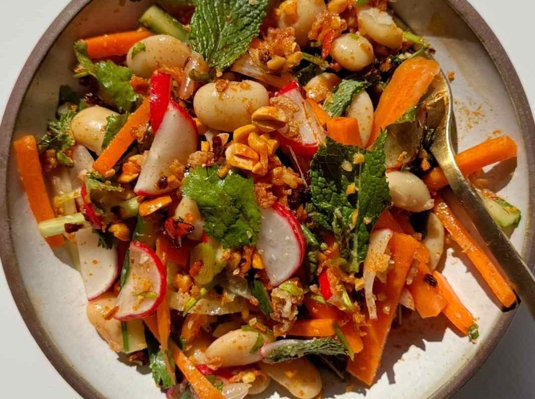 A butter bean salad with mint, cilantro, green onions, crushed peanuts, and fried shallots in a white bowl.