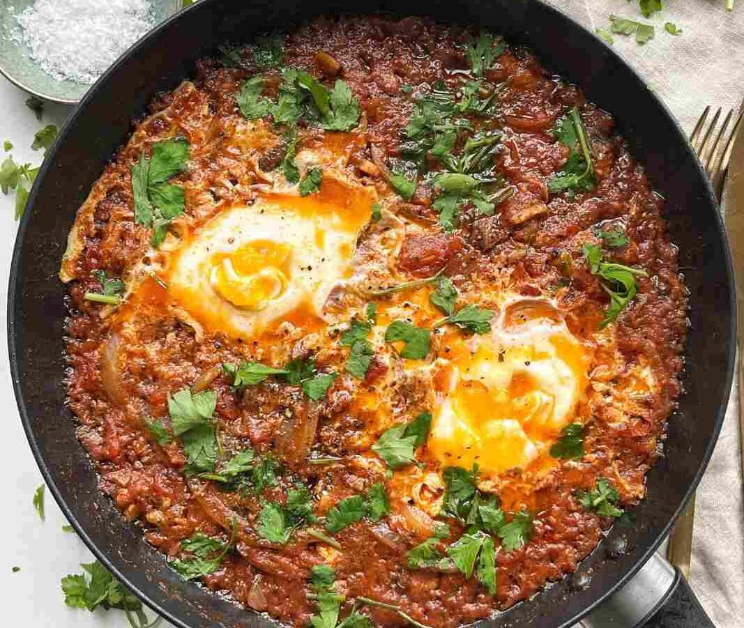A black pan full with of shakshuka-style dish of sardines broken into a spiced tomato base.