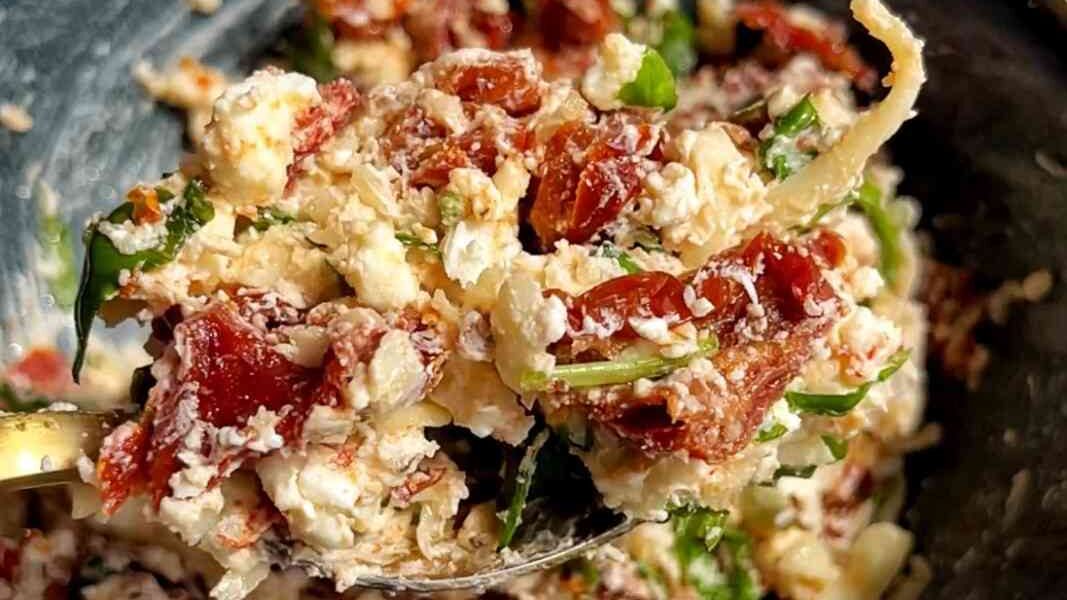 Bruschetta topping made with sun-dried tomatoes, basil, feta, cream cheese, and mozzarella, mixed together inside a black bowl.