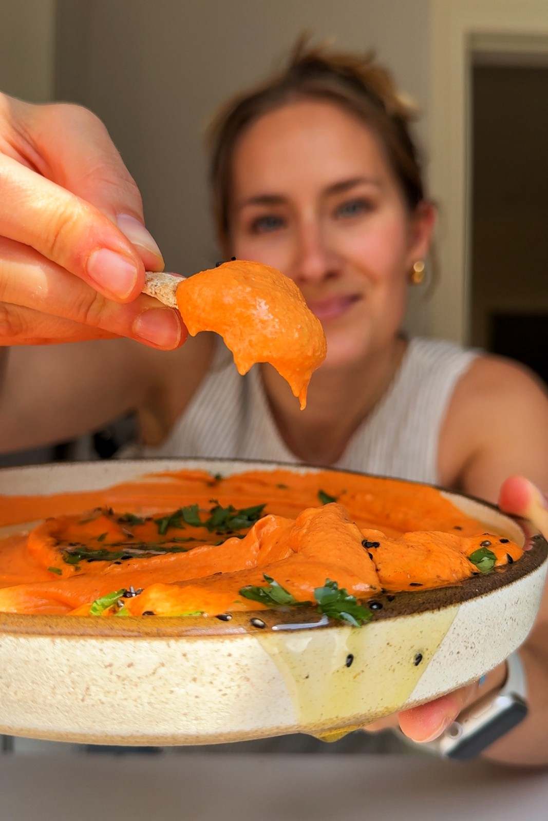 Emily dipping a cracker in her roasted red pepper hummus bruschetta topping.