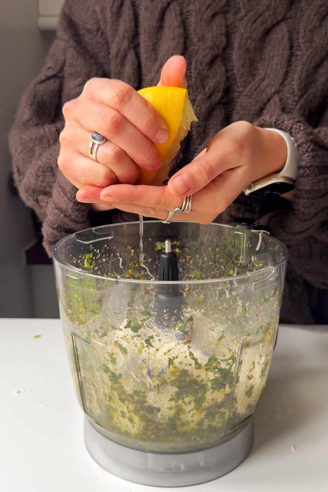 Emily squeezing a lemon into a blender full with pistachio pesto bruschetta topping.