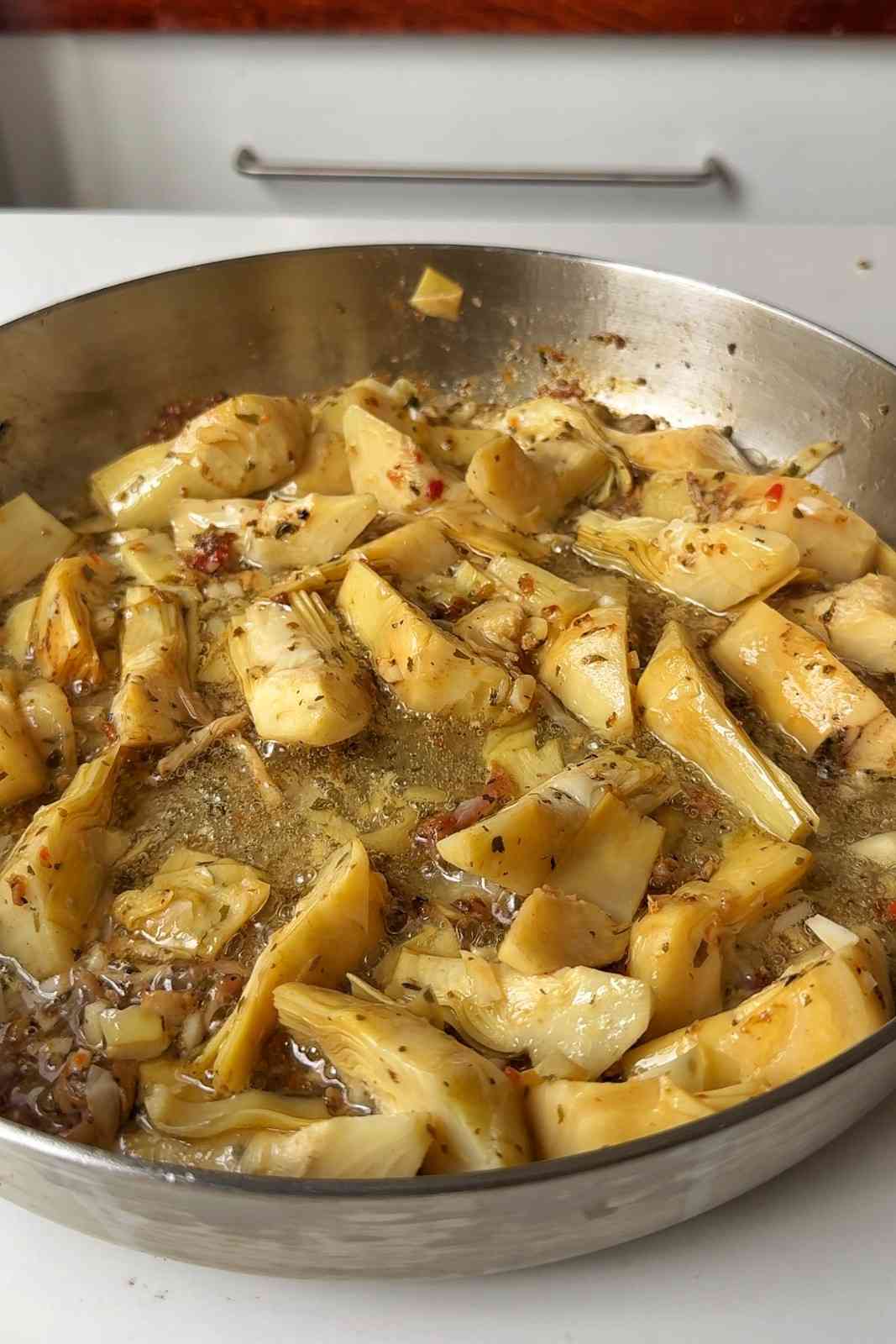 Artichoke hearts and chopped garlic sizzling in oil in the same skillet, flecked with herbs.
