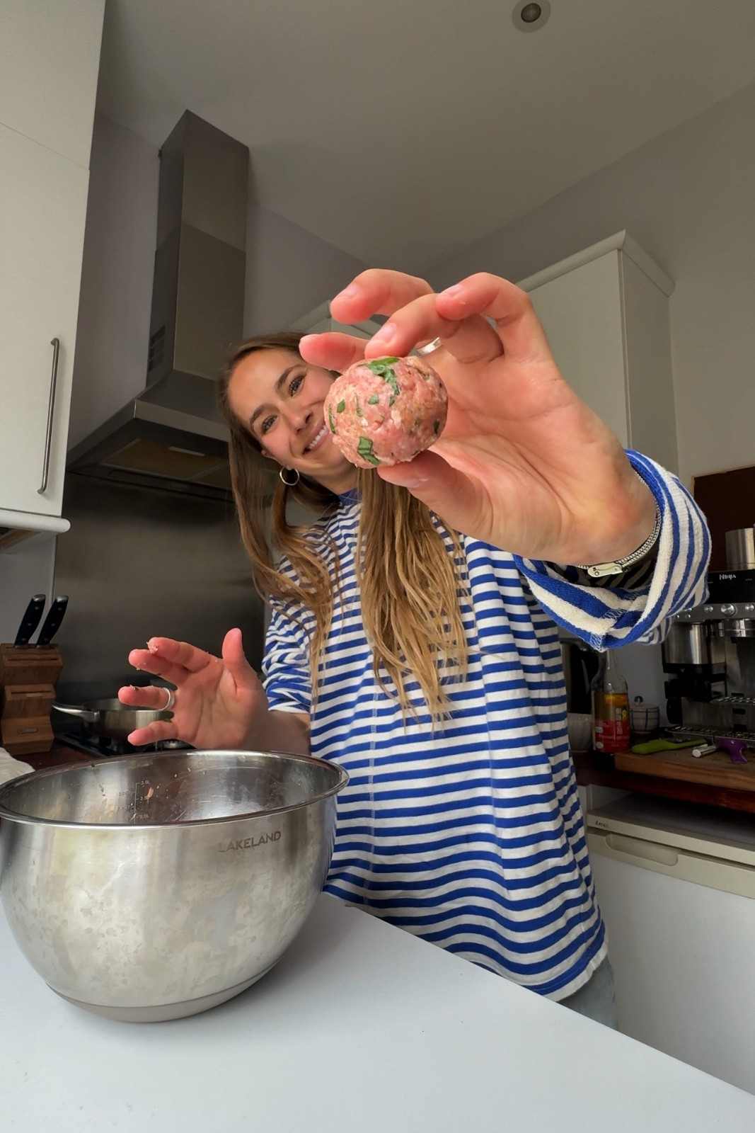 Emily holding up a raw pork meatball flecked with chopped parsley above a mixing bowl.