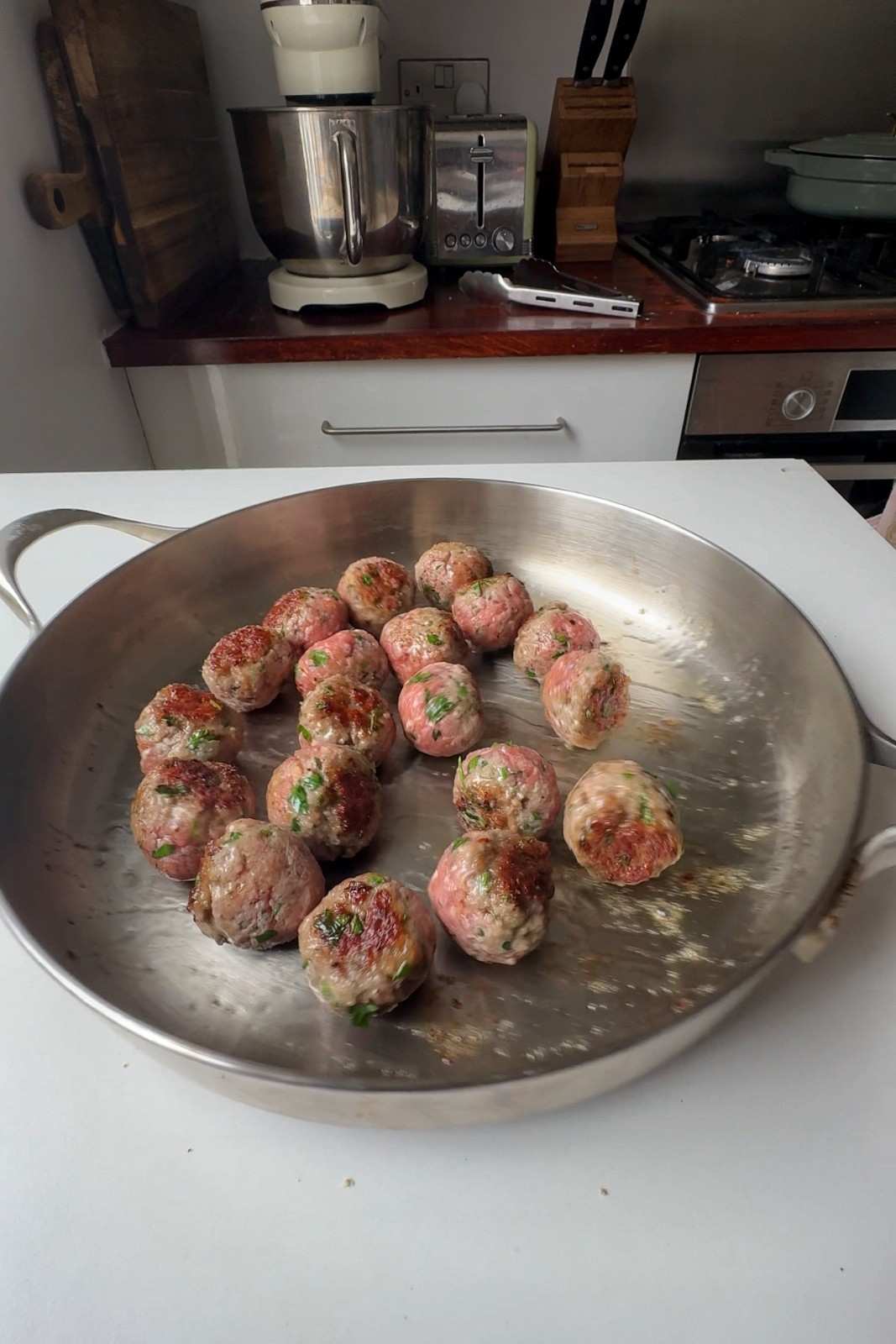 Pork meatballs searing in a stainless steel skillet, some turned to show their golden undersides.
