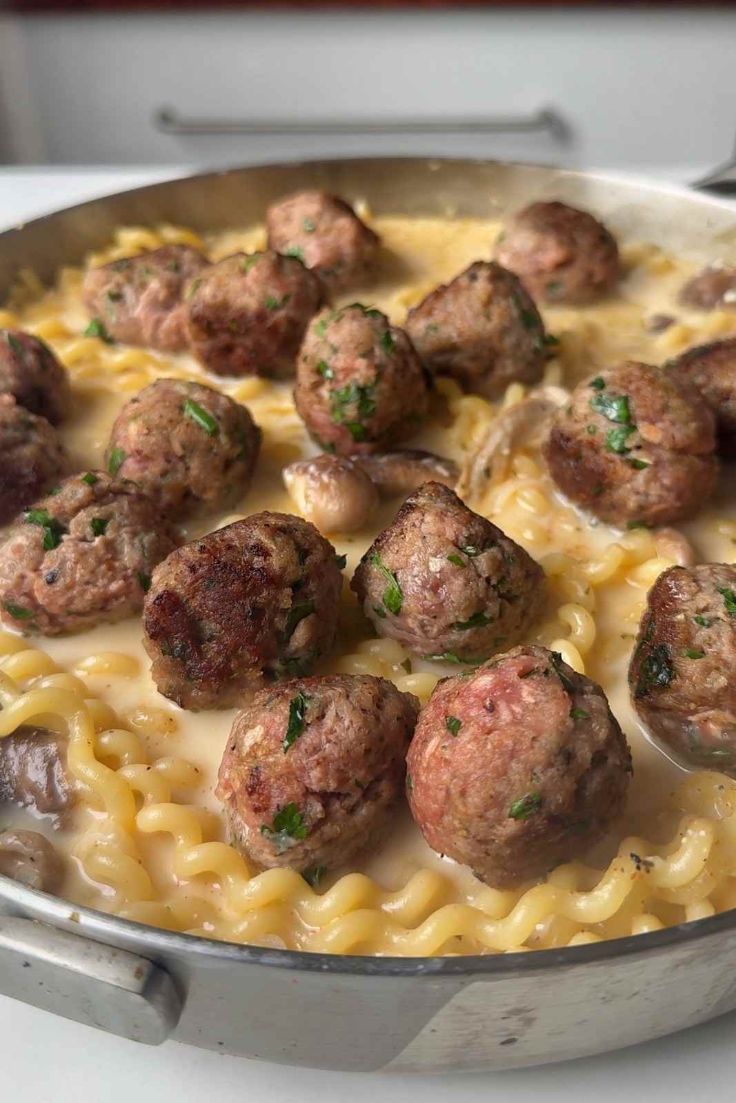 Browned pork meatballs nestled on top of pasta simmering in a creamy mushroom sauce.