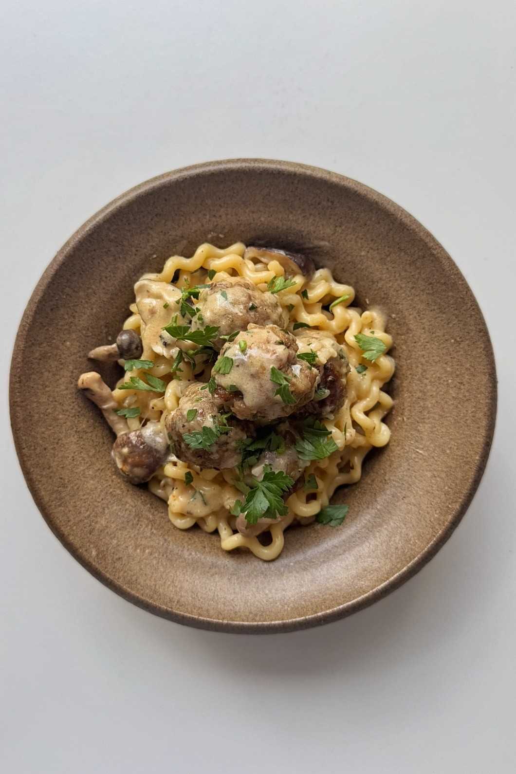 Overhead view of a bowl of long spiral pasta and pork meatballs in creamy mushroom sauce, topped with parsley.