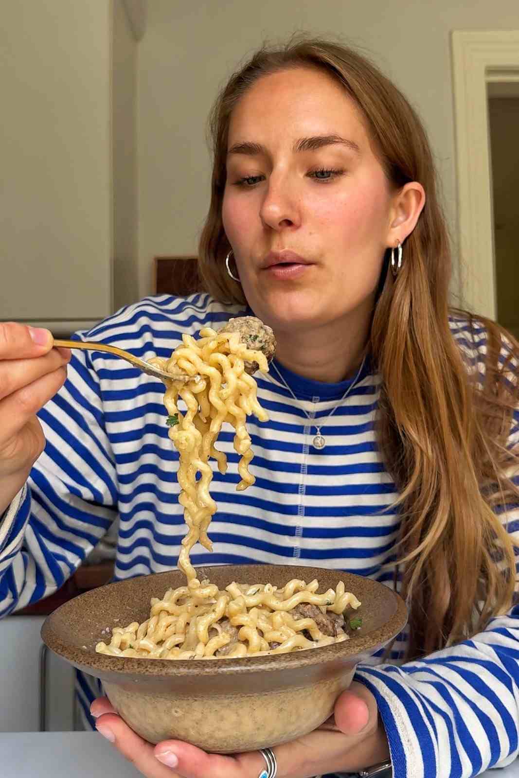 Emily Roz lifting a forkful of creamy pasta and a pork meatball from a stoneware bowl.