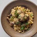 Overhead view of a bowl of long spiral pasta and pork meatballs in creamy mushroom sauce, topped with parsley.