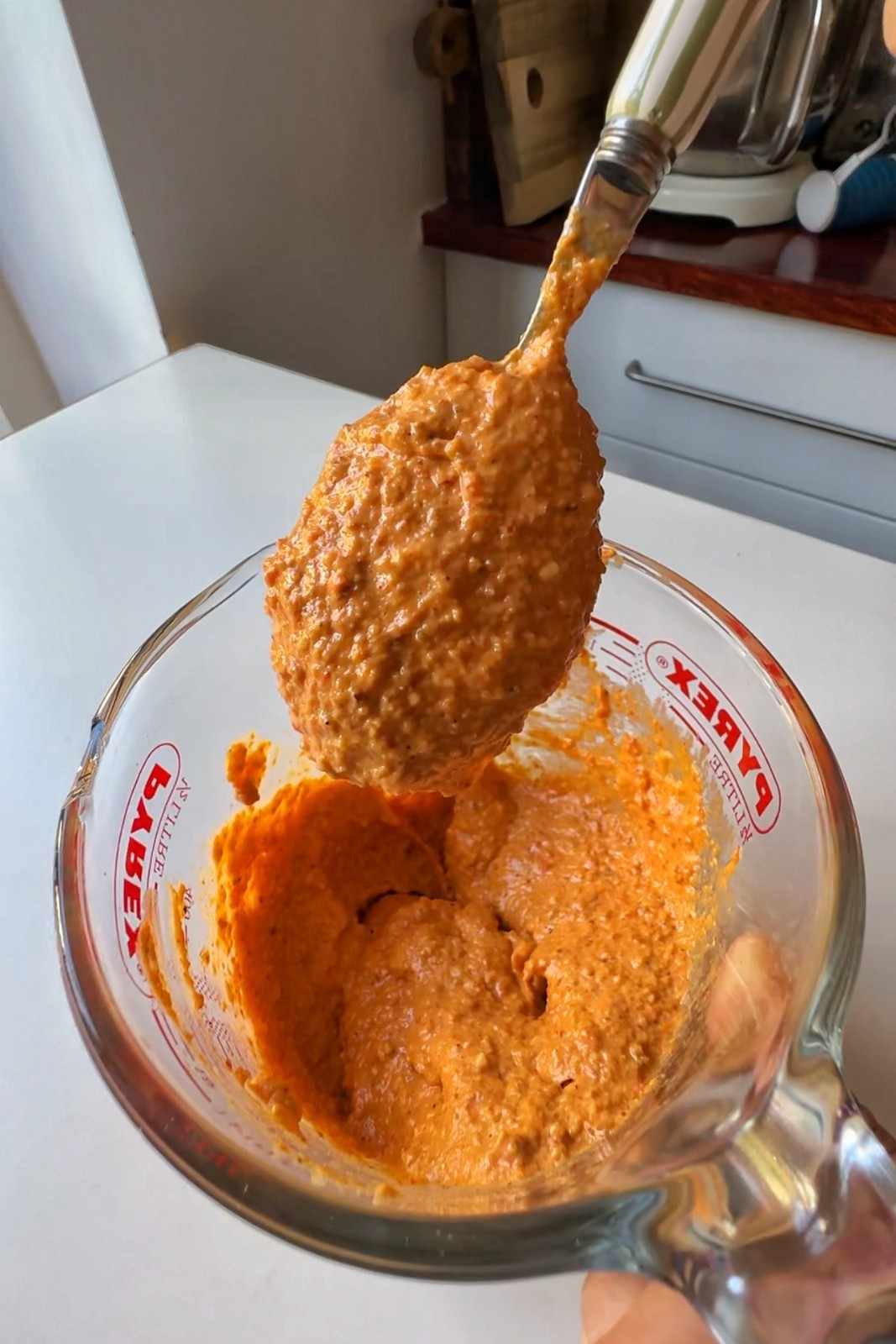 Spoonful of blended romesco sauce lifted from a glass measuring cup.
