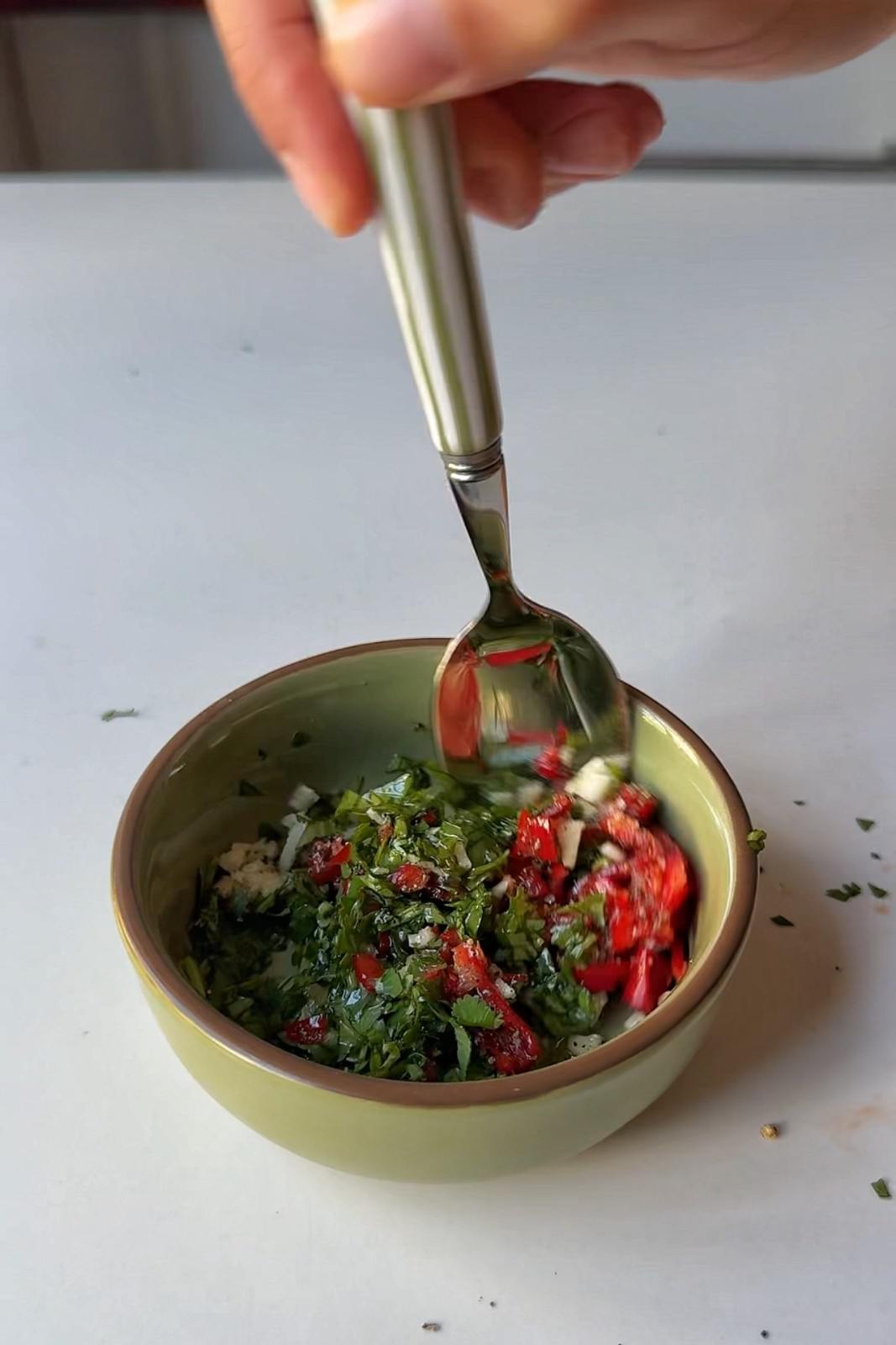 Cilantro, red chili and garlic green sauce being stirred together in a small green bowl.