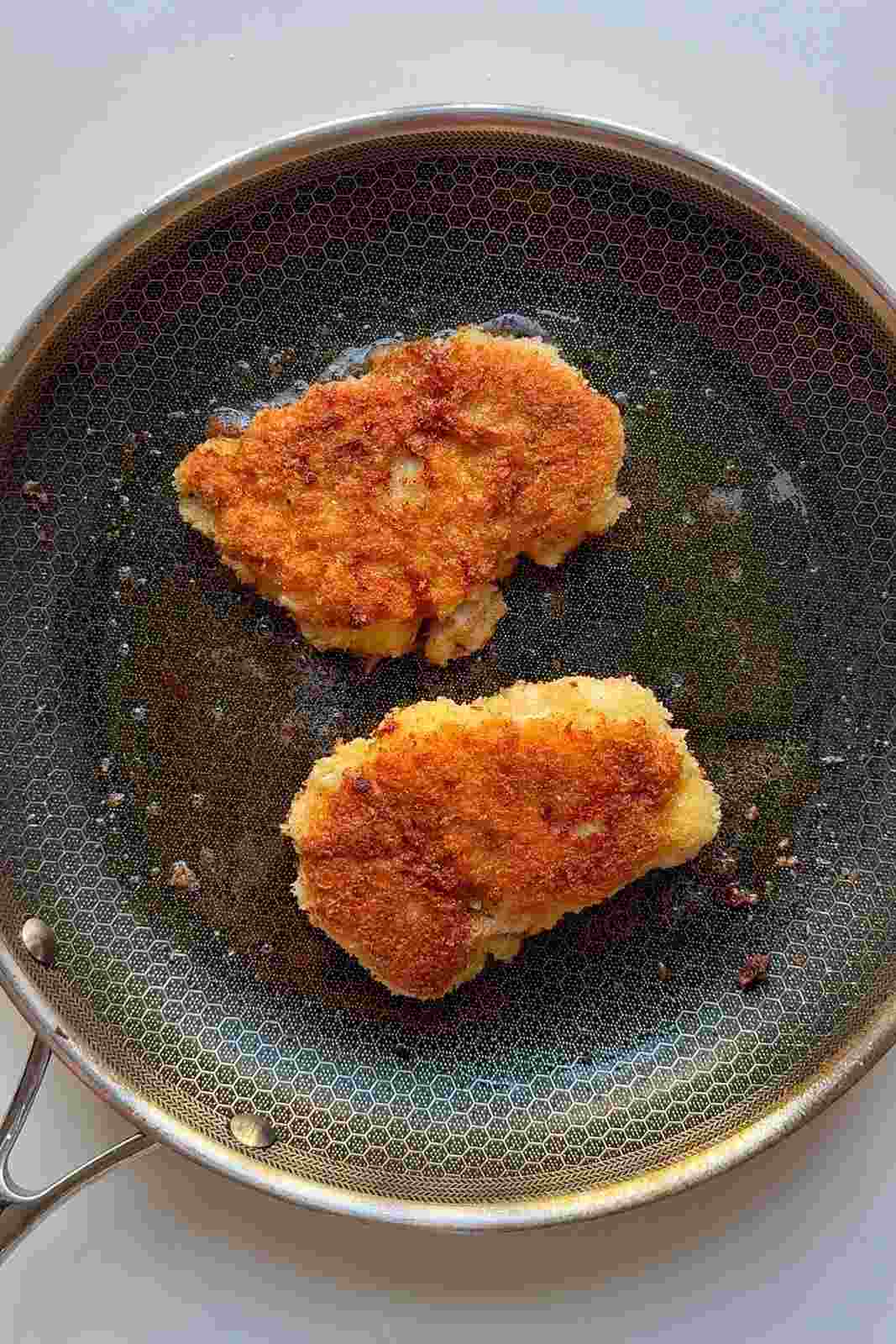 Two panko-coated chicken thighs frying to a deep golden brown in a skillet.