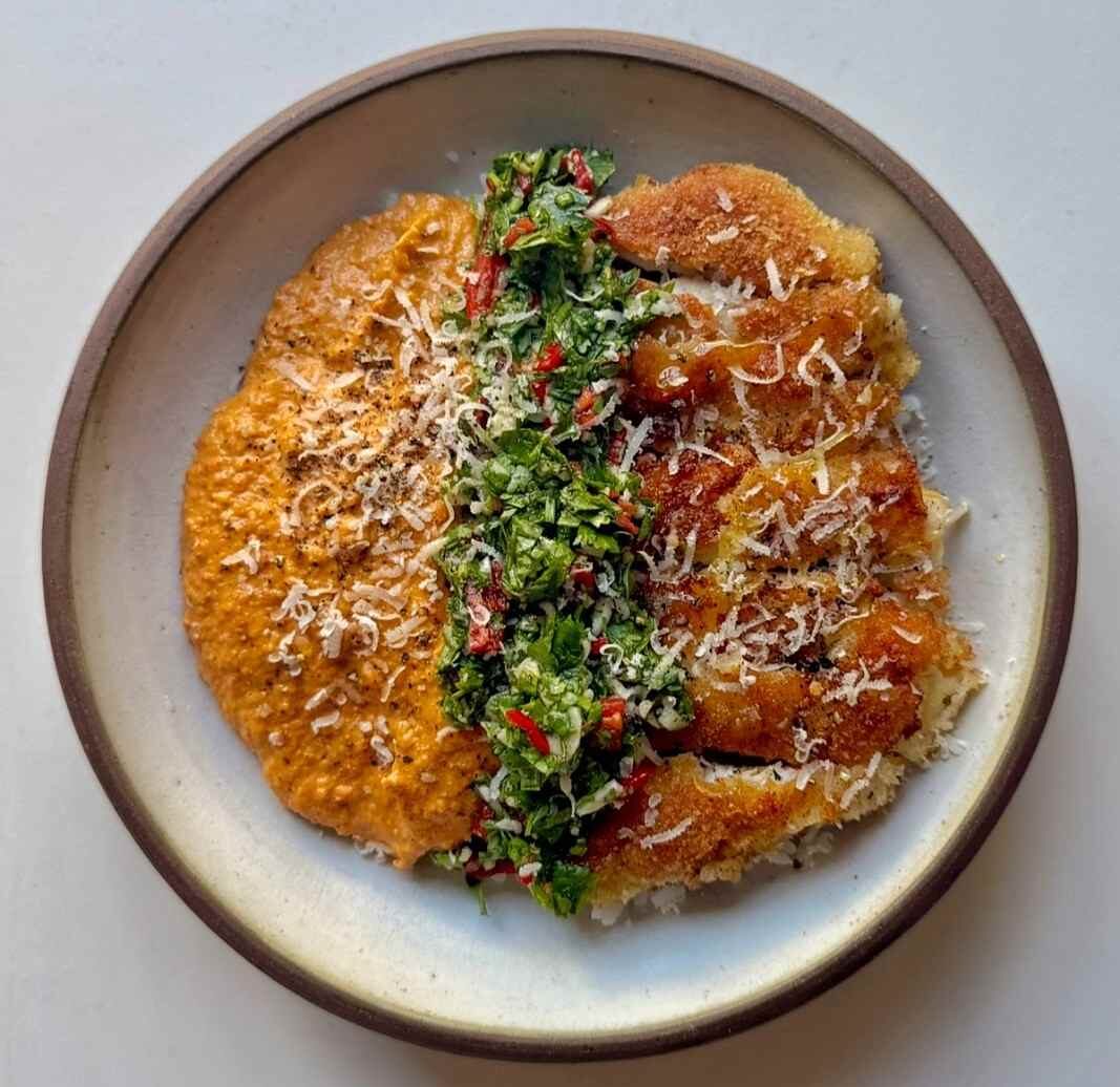 Overhead view of crispy romesco chicken over rice with romesco sauce, cilantro green sauce and grated parmesan.