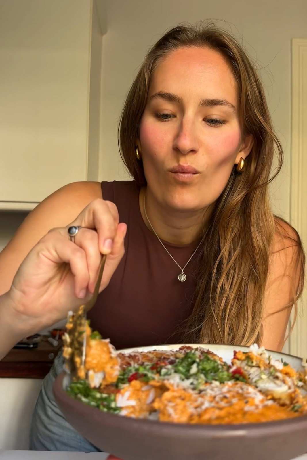 Emily eating a bowl of crispy romesco chicken with rice, romesco sauce and green sauce.
