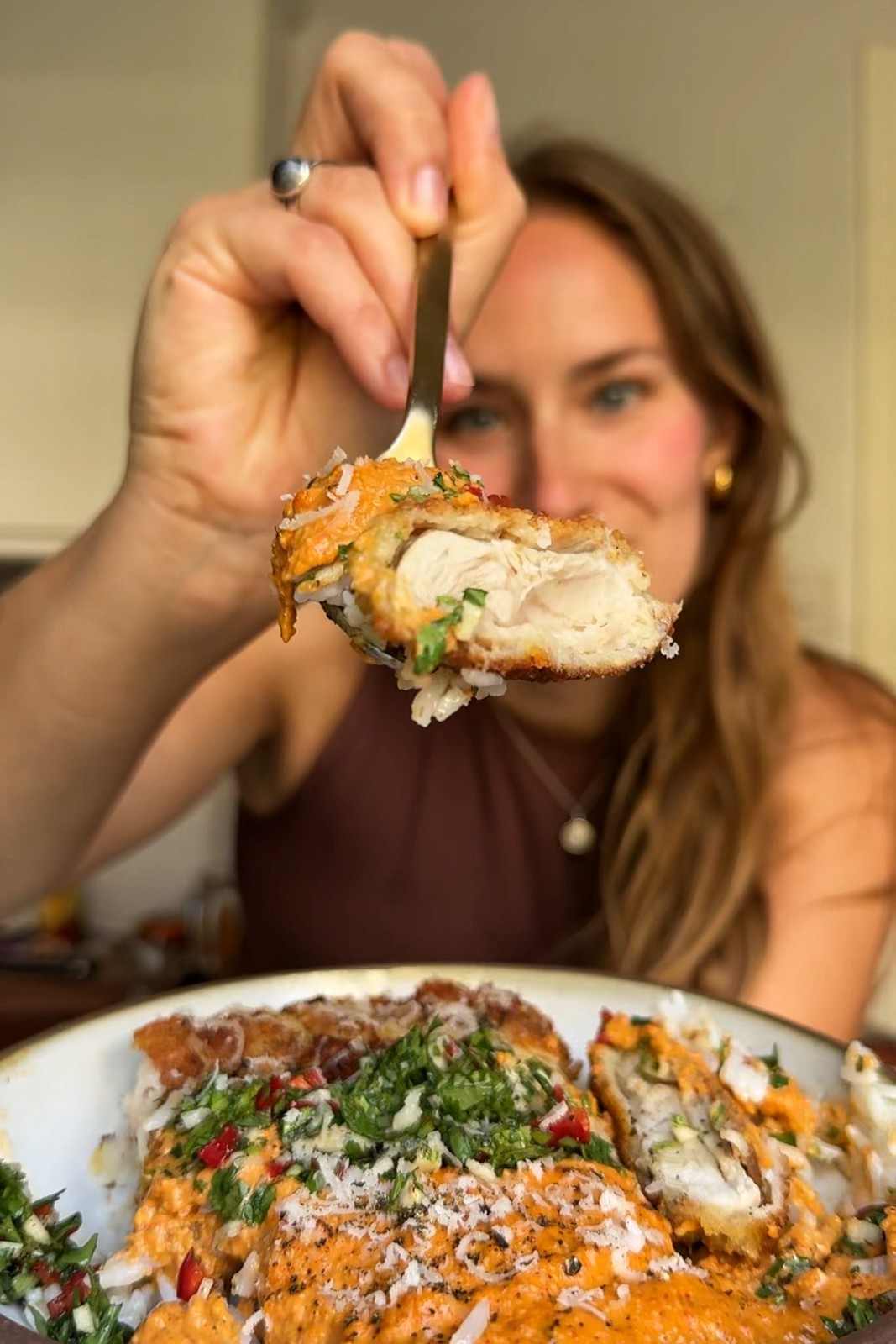 Emily Roz holding up a forkful of crispy romesco chicken, showing the juicy chicken inside the panko crust.