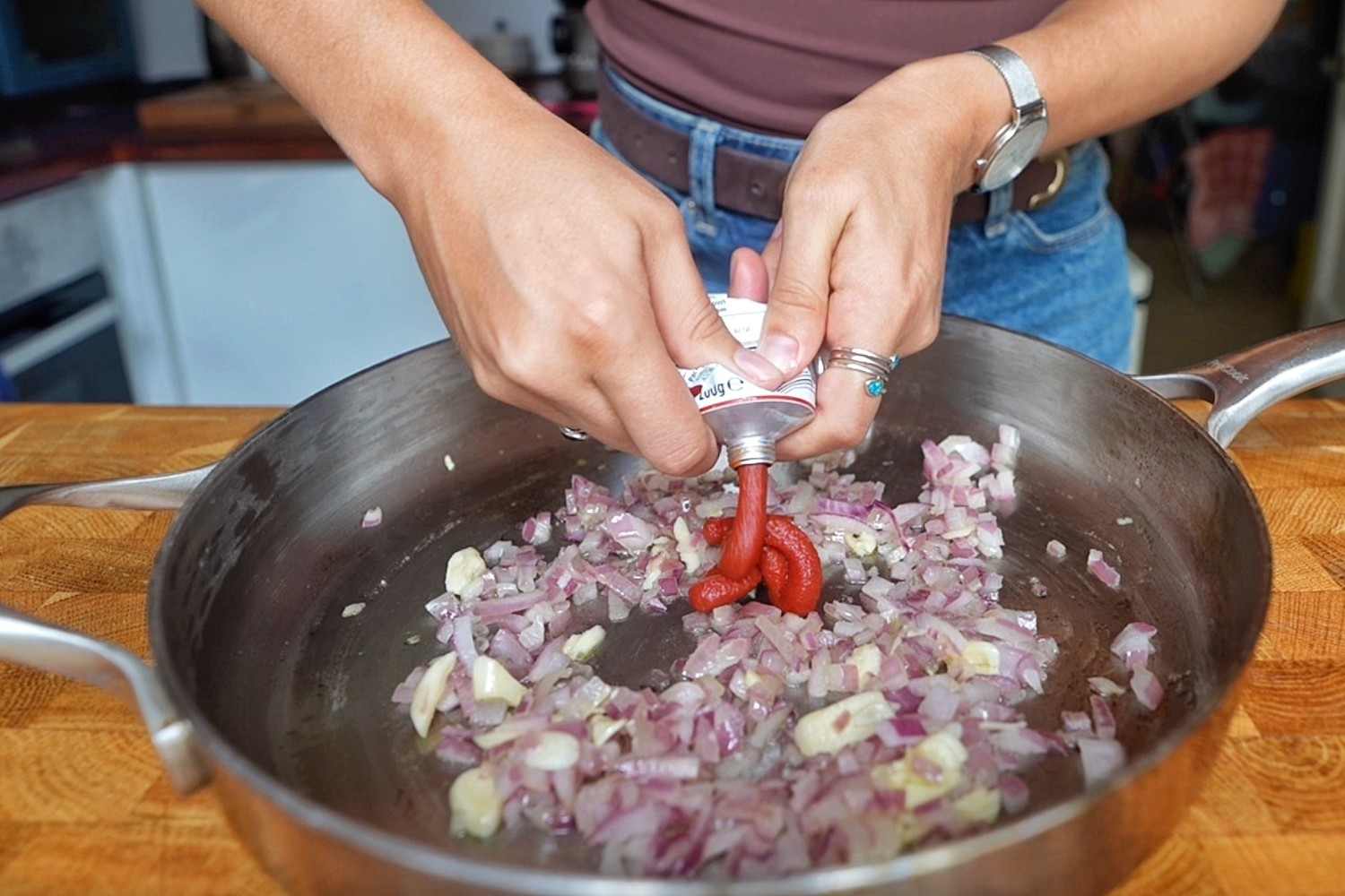 Emily squeezing tomato paste from a tube into a pan of softened red onion and garlic.