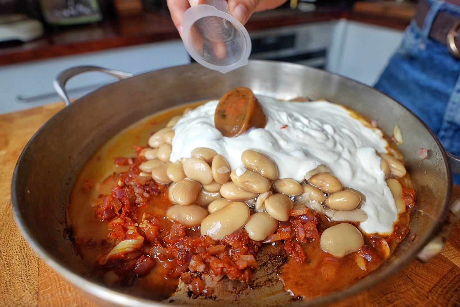 Emily adding vegetable stock to a pan of butter beans, blended silken tofu and spiced tomato base.