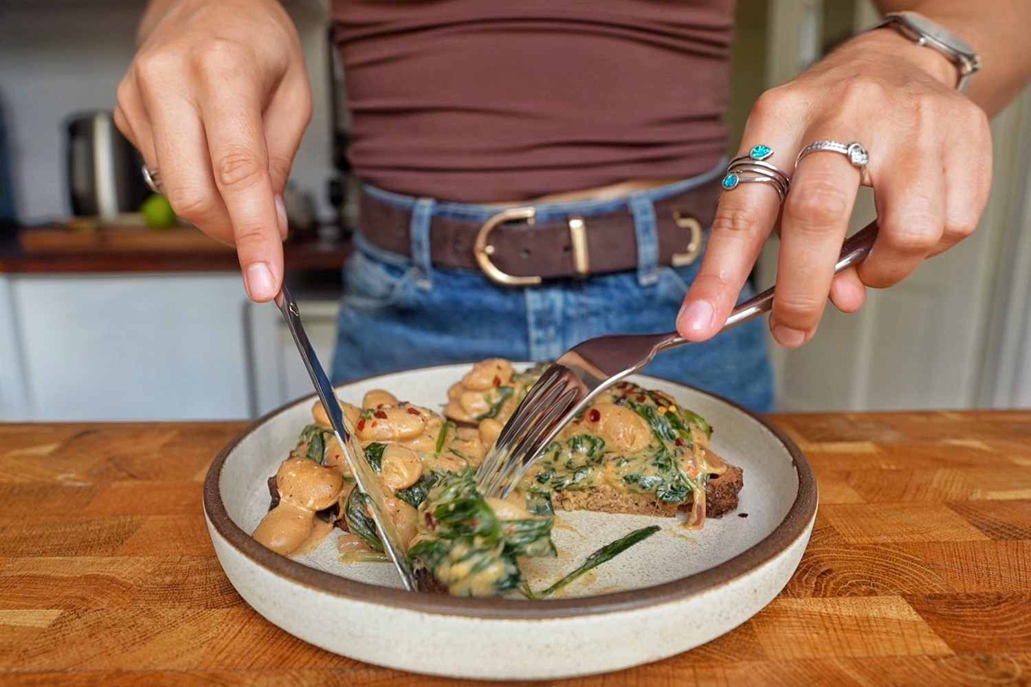 Cutting into creamy curried butter beans on toasted sourdough with a knife and fork.