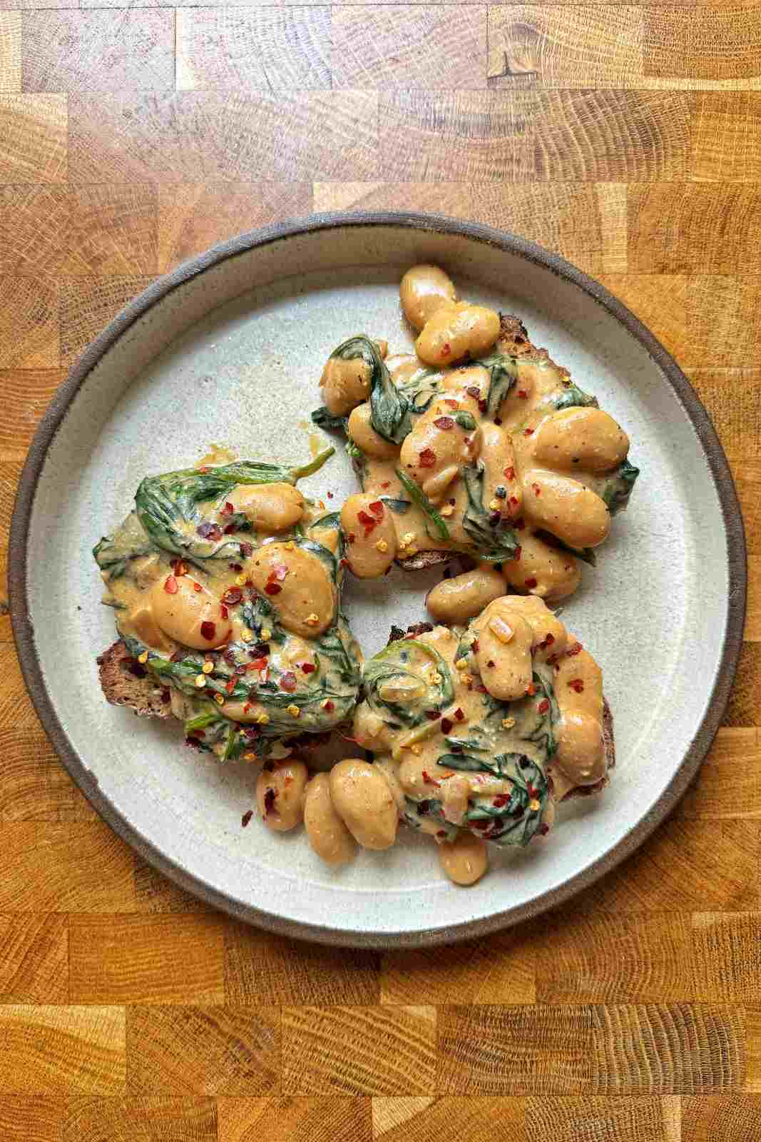 Overhead view of creamy curried butter beans with spinach on two slices of sourdough toast, scattered with red pepper flakes.