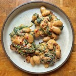 Overhead view of creamy curried butter beans with spinach on two slices of sourdough toast, scattered with red pepper flakes.