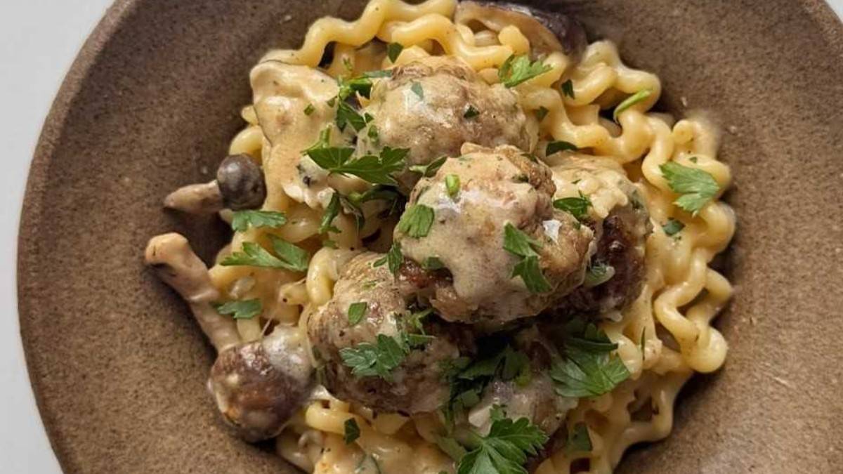 Overhead view of a bowl of long spiral pasta and pork meatballs in creamy mushroom sauce, topped with parsley.