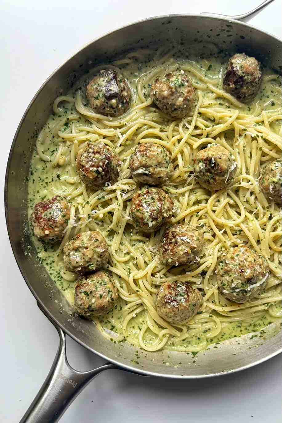 Creamy pesto pasta and meatballs in a stainless steel skillet.