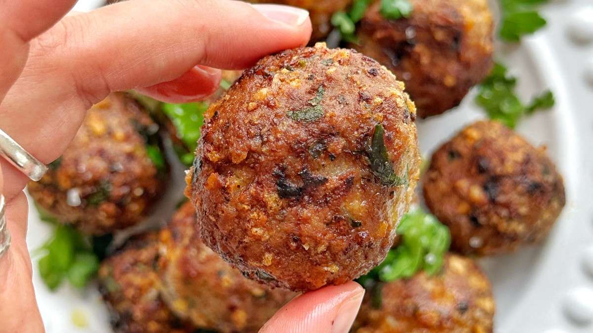 Emily Roz holding up one of her air fryer turkey meatballs above a white plate.