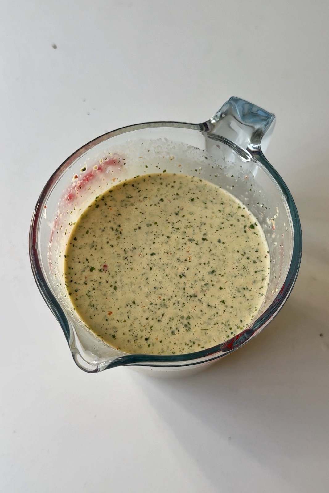 Blended lime leaf, cilantro and coconut milk marinade in a glass measuring jug, pale green with herb flecks.