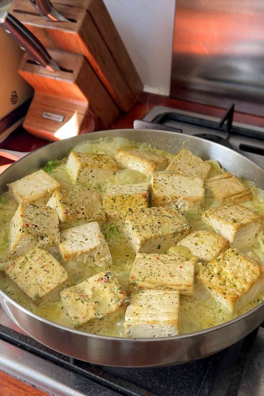 Baked tofu cubes simmering in the leftover coconut marinade on top of fried cabbage in a large skillet on the stove.