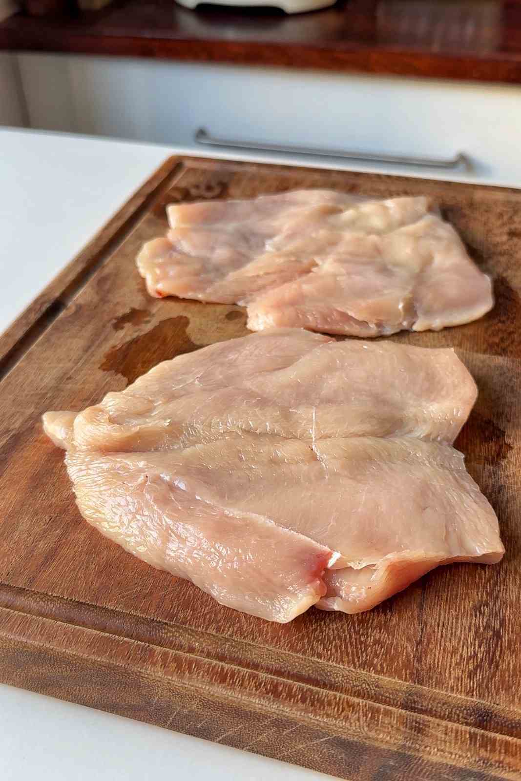 Two butterflied chicken breasts, bashed thin and even, on a wooden cutting board.