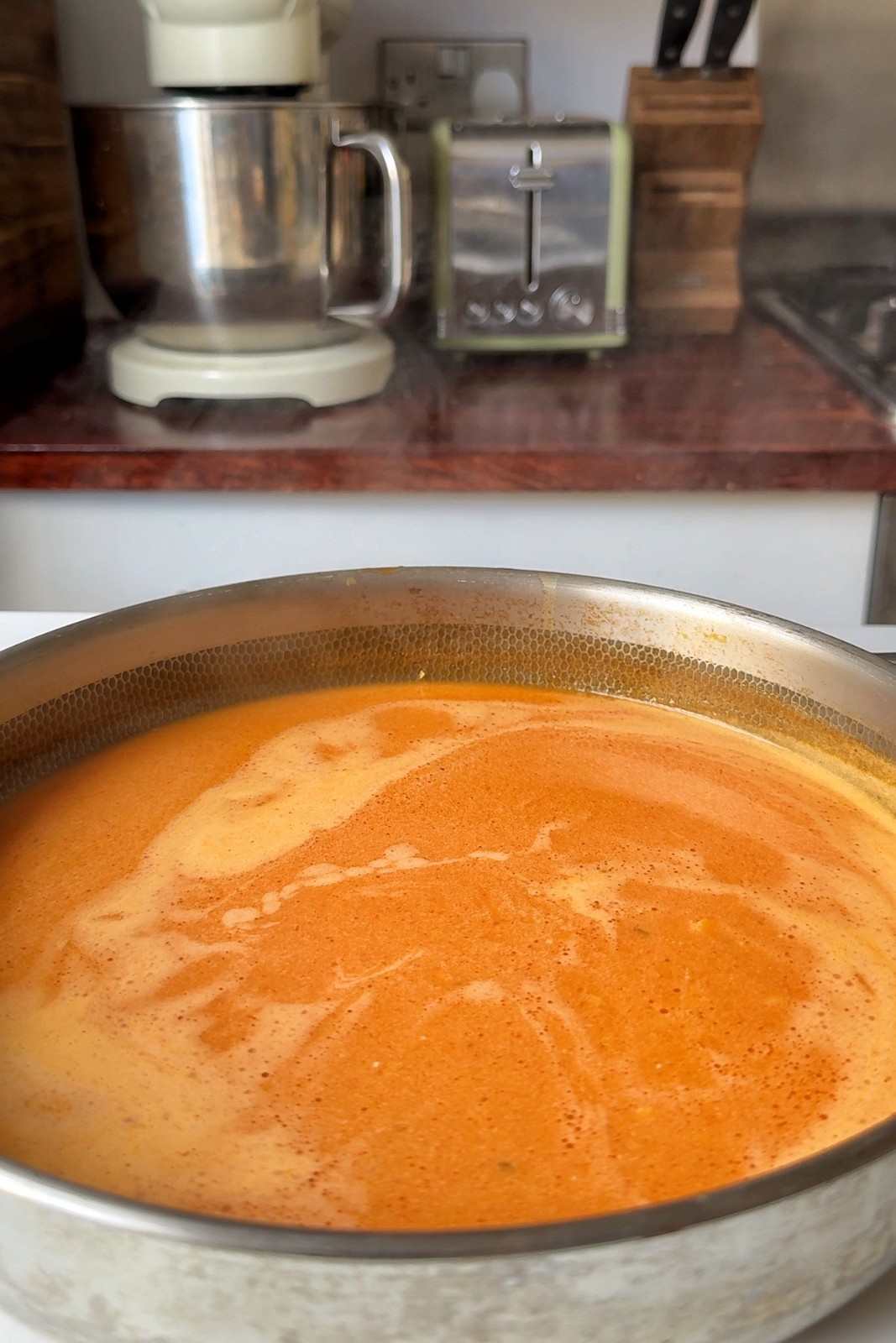 Creamy orange gochujang sauce made with cream and chicken stock in a large stainless steel skillet, ready for the pasta.