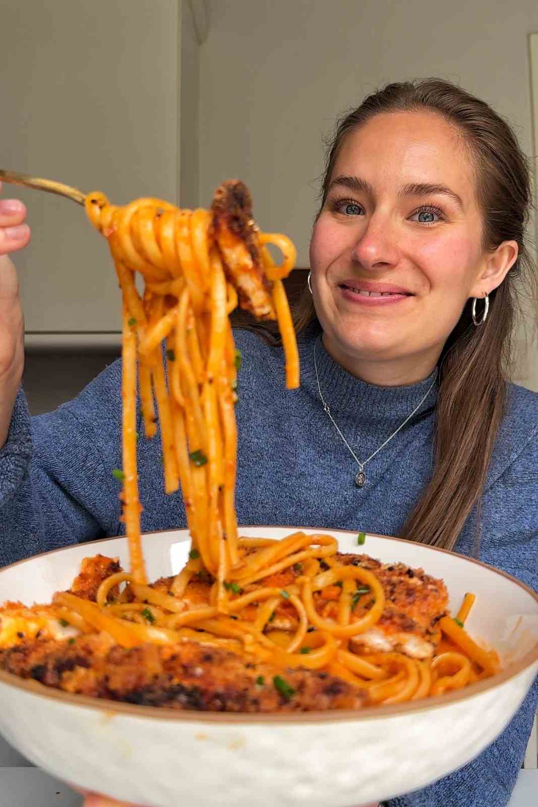 Emily Roz lifting a forkful of creamy gochujang linguine and crispy chicken from a bowl of Korean fried chicken pasta.