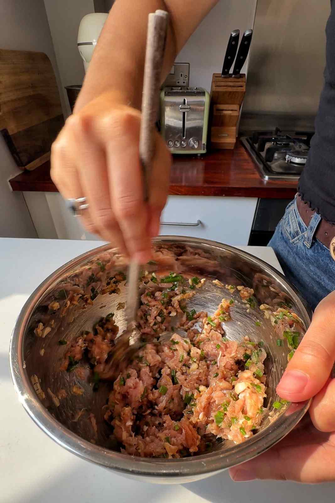 Emily Roz stirring ground chicken, chives, ginger and garlic together with chopsticks in a stainless steel mixing bowl.
