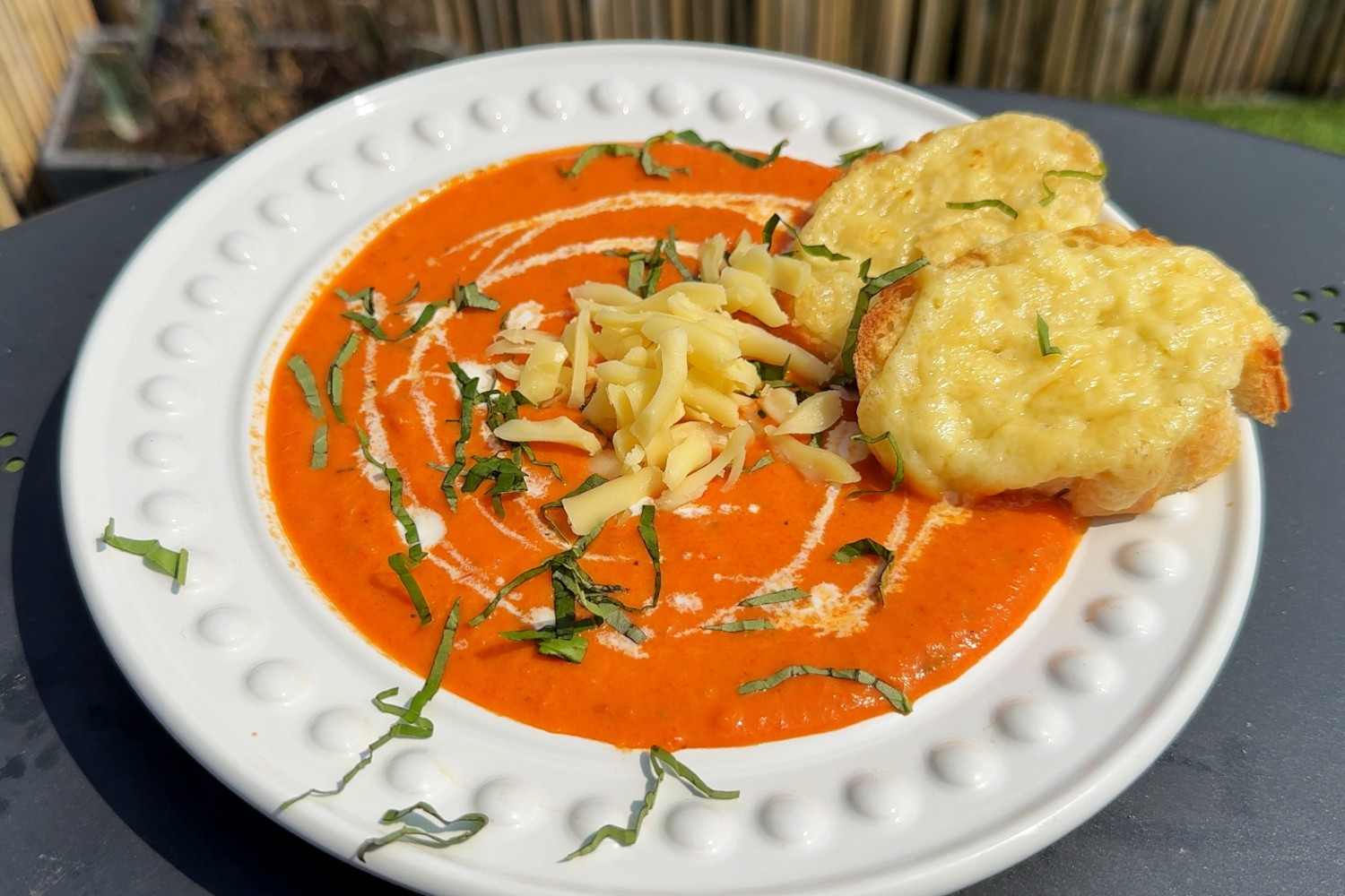 A bowl of roasted red pepper and gouda soup with a swirl of cream in the center.
