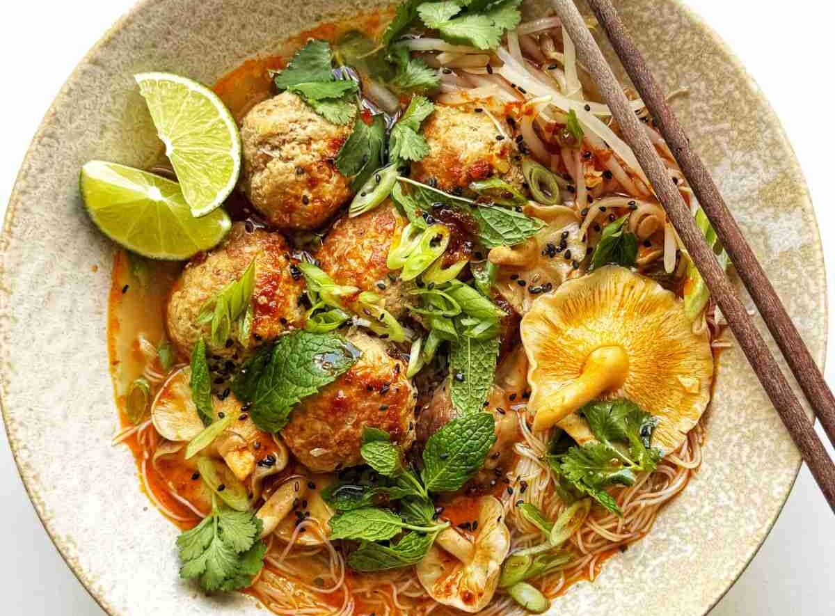 Fresh mint, cilantro, and scallion as a garnish on a bowl of Thai-style pork meatball soup.
