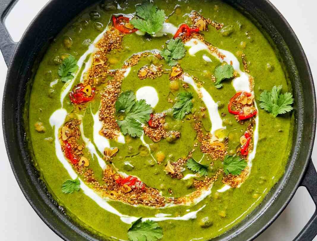 A tadka made of cumin seeds, mustard seeds, sliced garlic, and sliced red chilies, on top of a spinach dal.