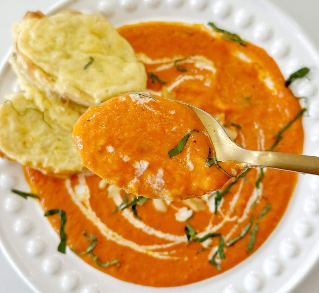 A spoonful of roasted red pepper and gouda soup with a swirl of cream, one of my favorite soup toppings.
