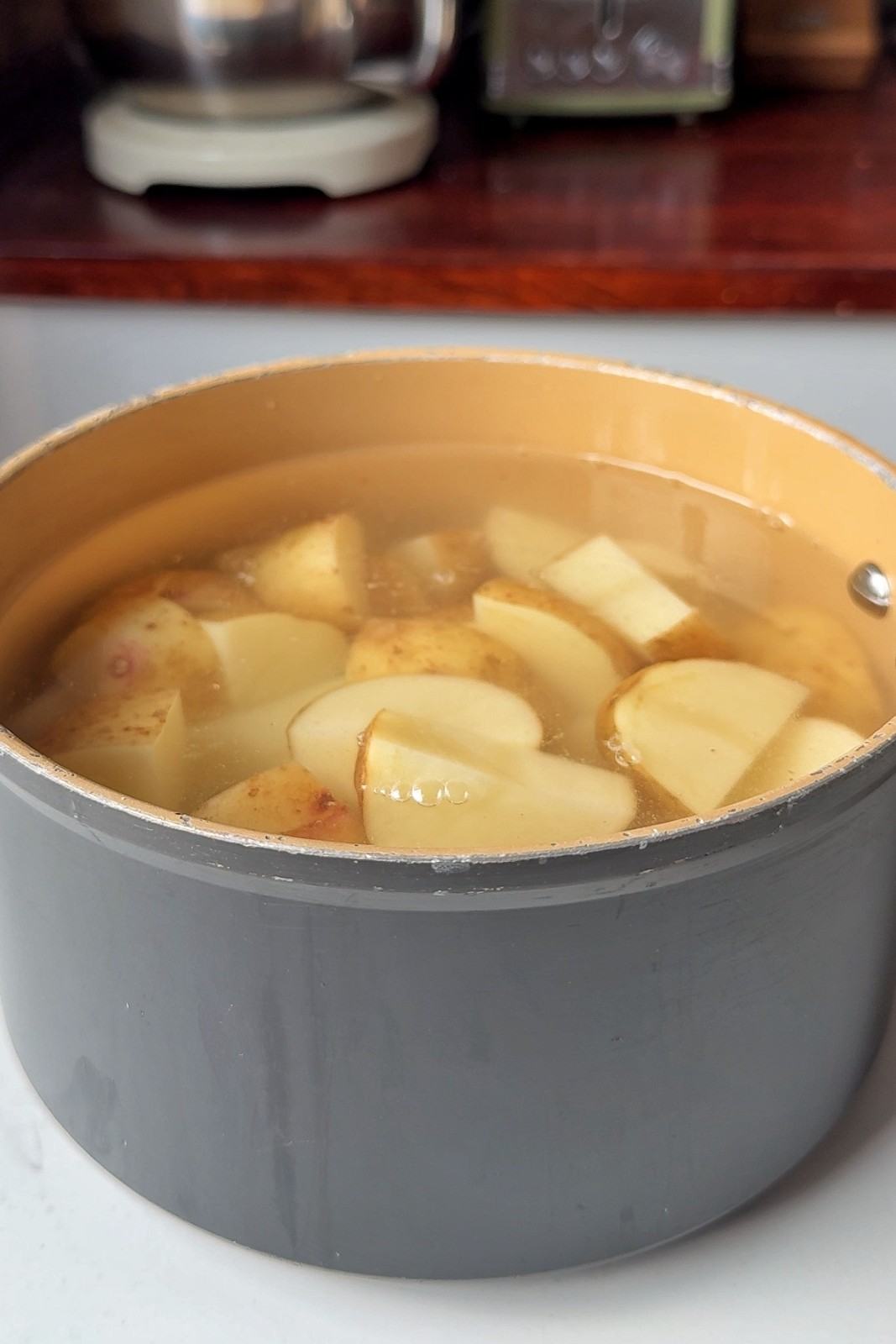Chunks of skin-on potatoes covered with water in a saucepan, ready to boil for mashed potatoes.