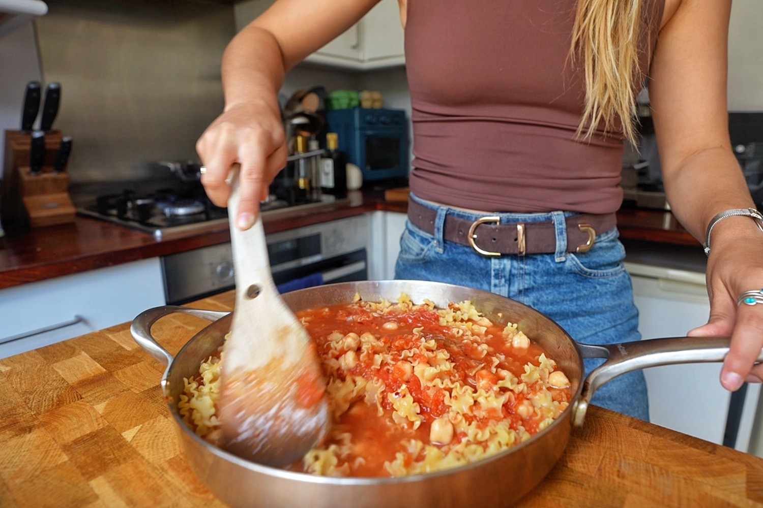 Stirring canned tomatoes into pasta and chickpeas in a stainless steel skillet.