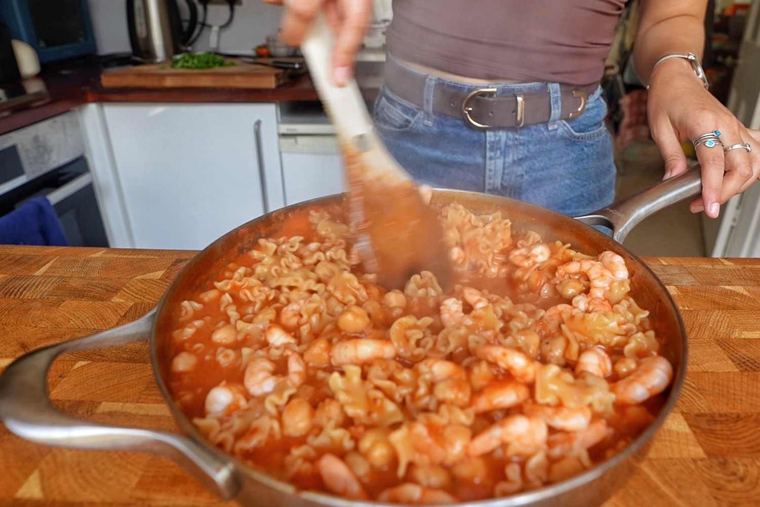 Stirring raw shrimp into one pot tomato pasta with chickpeas in a skillet.