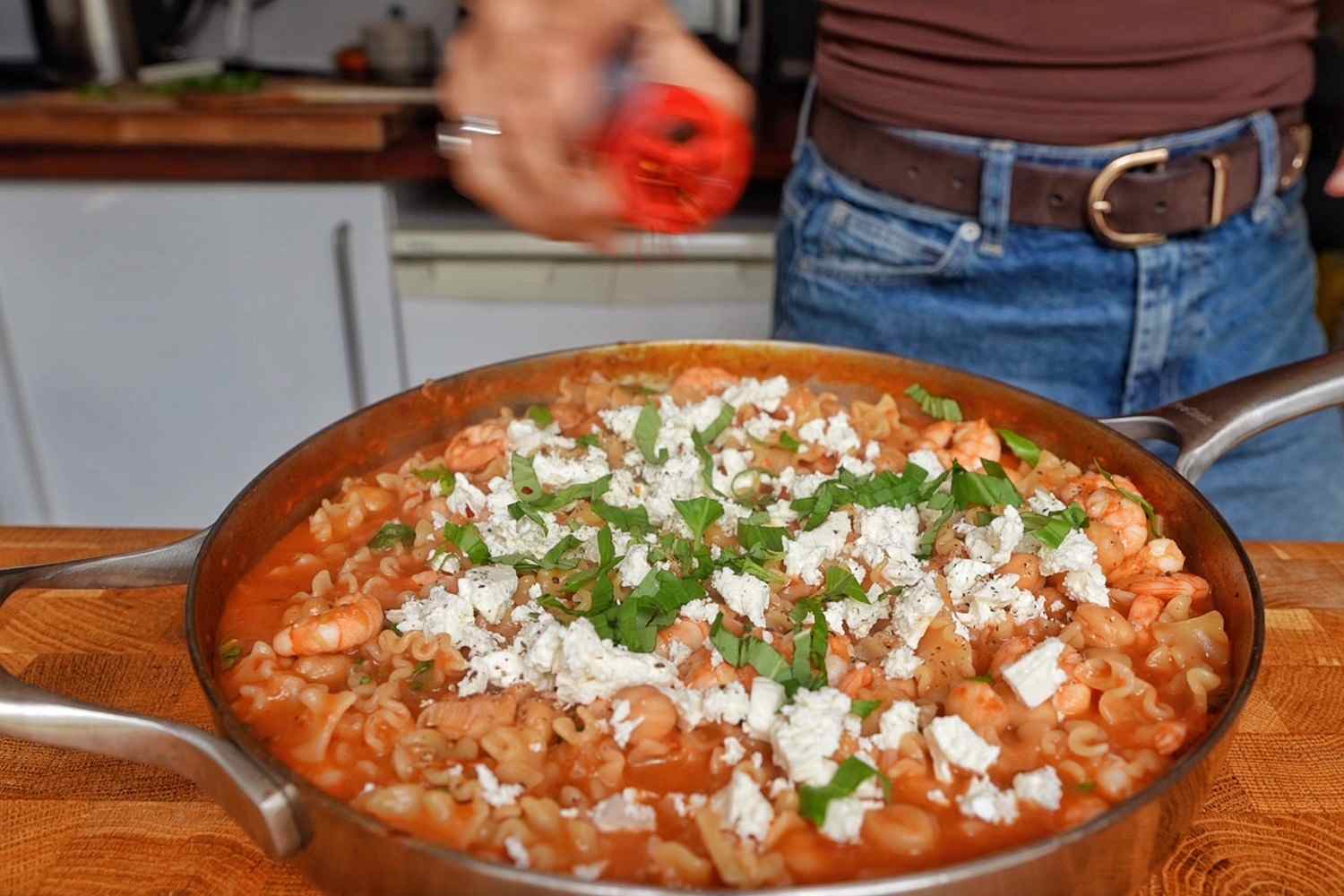 Crumbled feta and chopped fresh basil scattered over a skillet of tomato shrimp pasta.