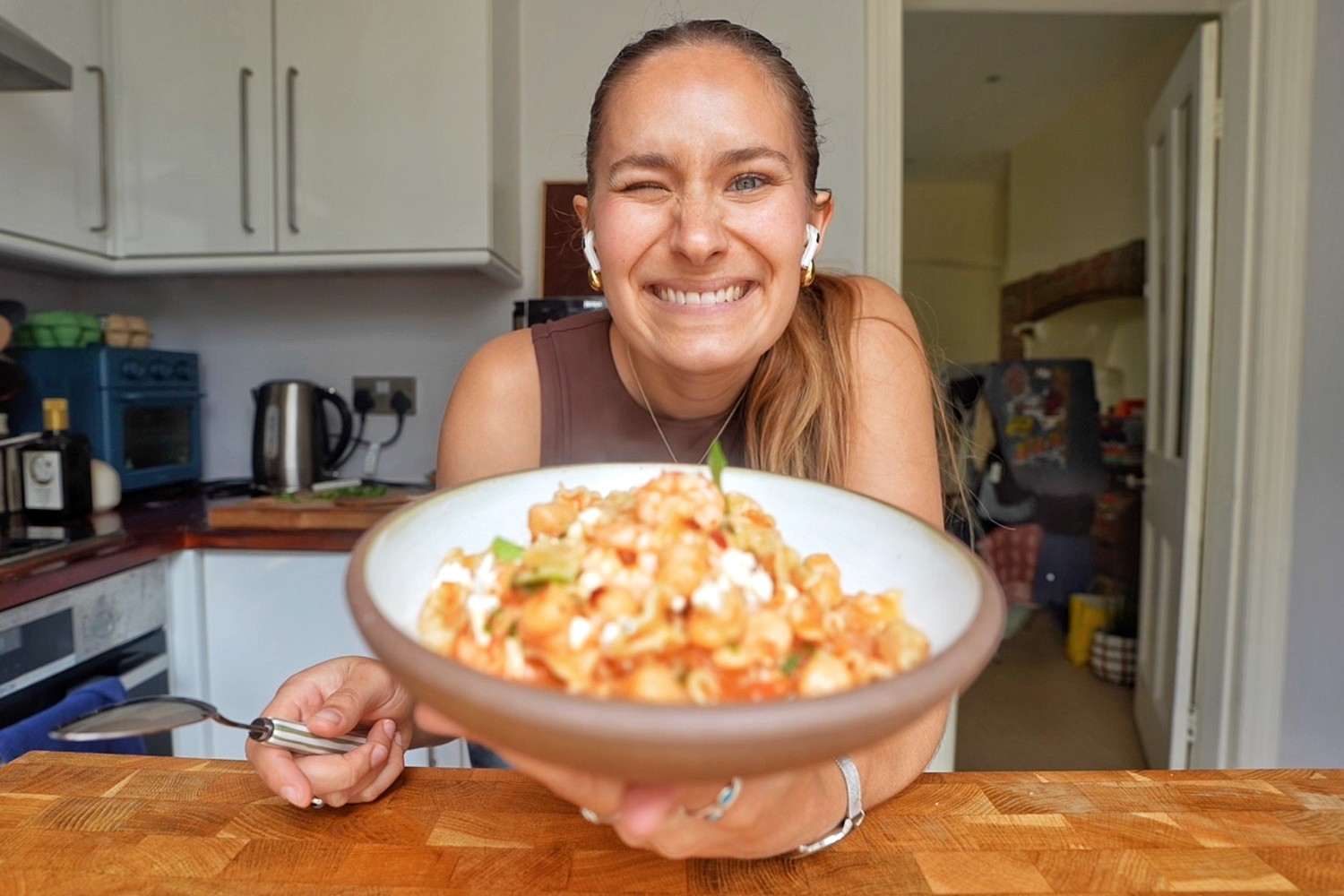 Emily holding a bowl of one pot tomato shrimp pasta topped with feta and basil.