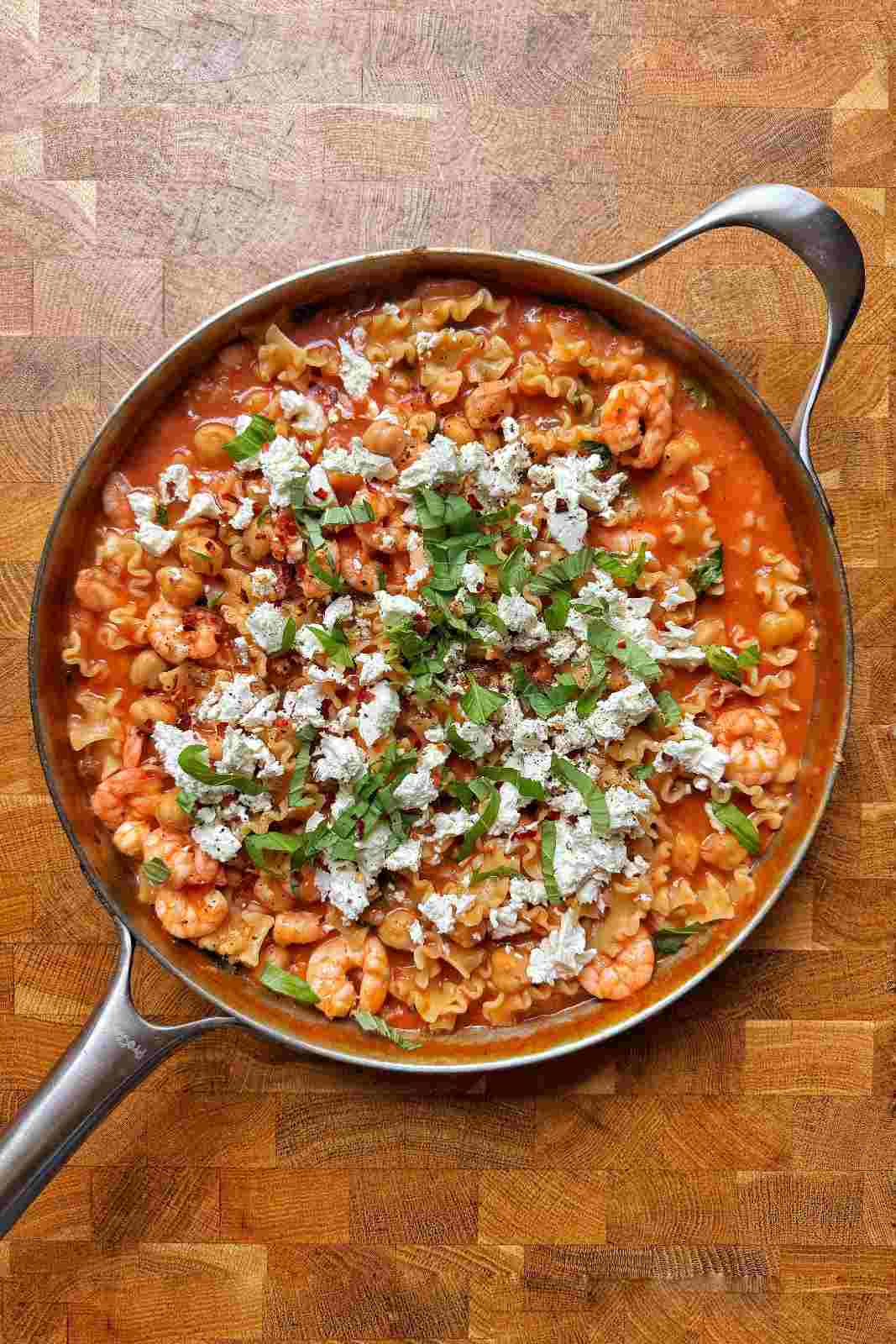 Overhead view of one pot tomato shrimp pasta in a skillet with chickpeas, crumbled feta and fresh basil.