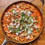 Overhead view of one pot tomato shrimp pasta in a skillet with chickpeas, crumbled feta and fresh basil.